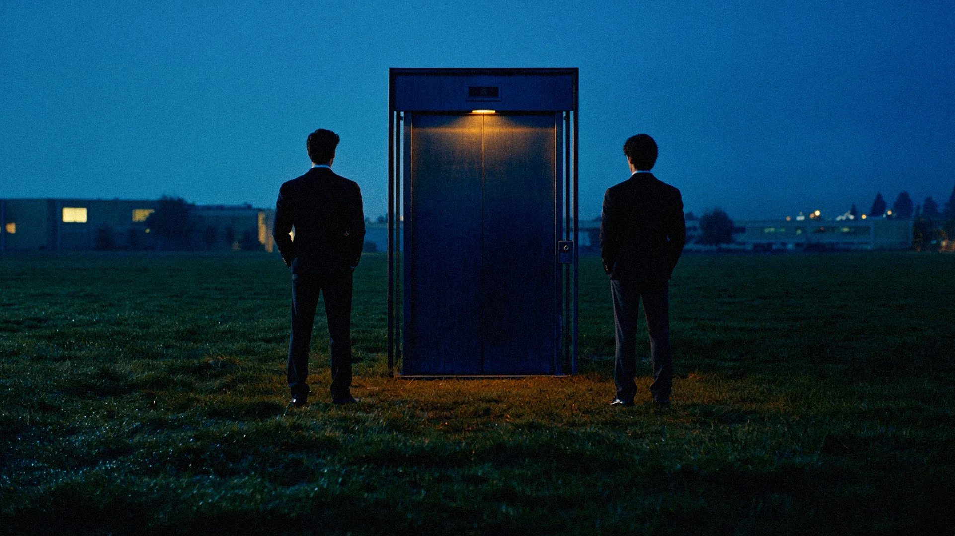 Arian and Caleb seen from behind, standing far apart on either side of the elevator on the dusky lawn